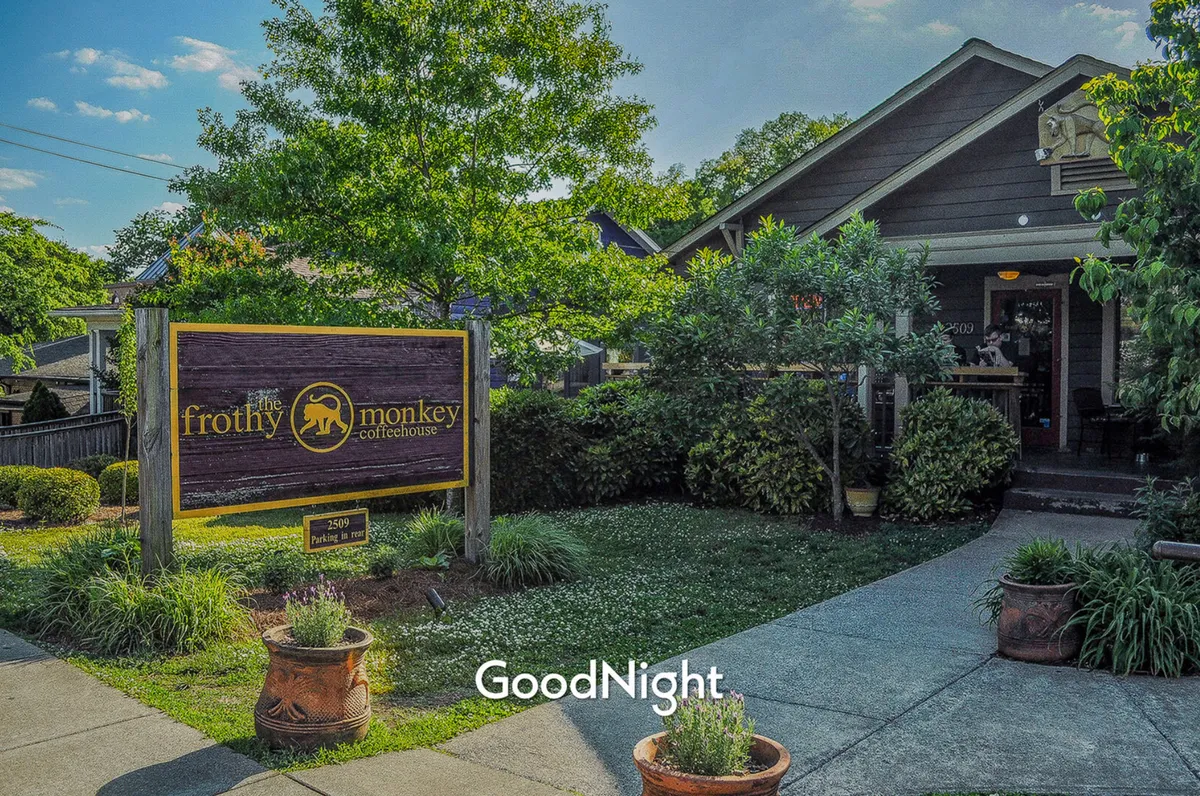 The image displays a charming coffeehouse entrance surrounded by greenery, with a welcoming sign that hints at expertly crafted coffee and a relaxed, community-oriented atmosphere. The scene suggests opportunities to unwind and socialize.