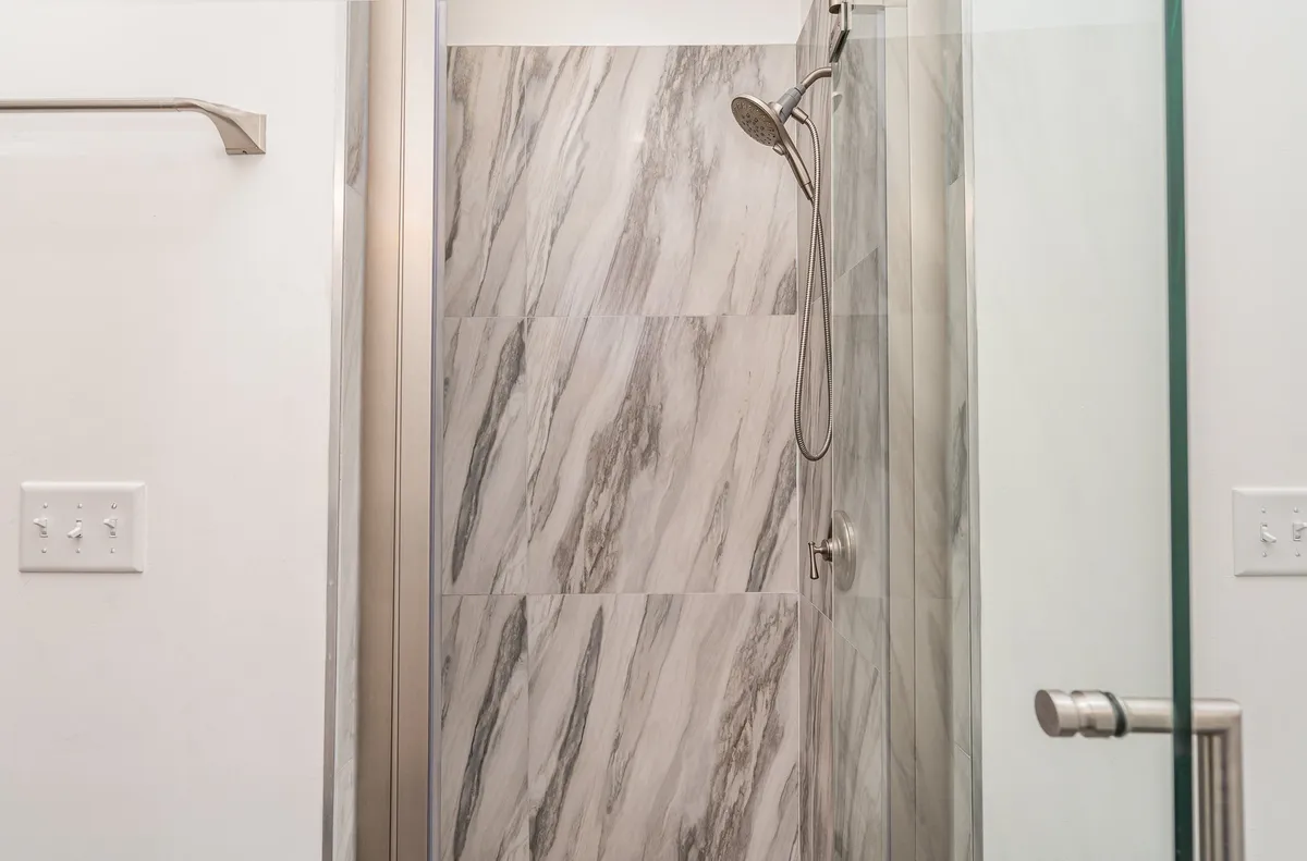 A luxurious walk-in shower with marble walls, a glass door, and a sleek showerhead. The clean lines and spa-like atmosphere evoke a sense of indulgence and relaxation.