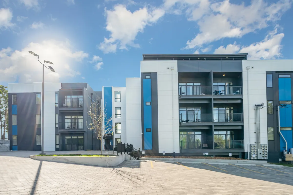 This exterior image highlights a modern building facade with striking blue accents and multiple balconies, set against a clear sky. The balconies are equipped with outdoor furniture, suggesting spaces for relaxation and social gatherings. The mood is welcoming and contemporary, embodying the inviting atmosphere of Gallatin Retreat and its communal, family-friendly orientation.