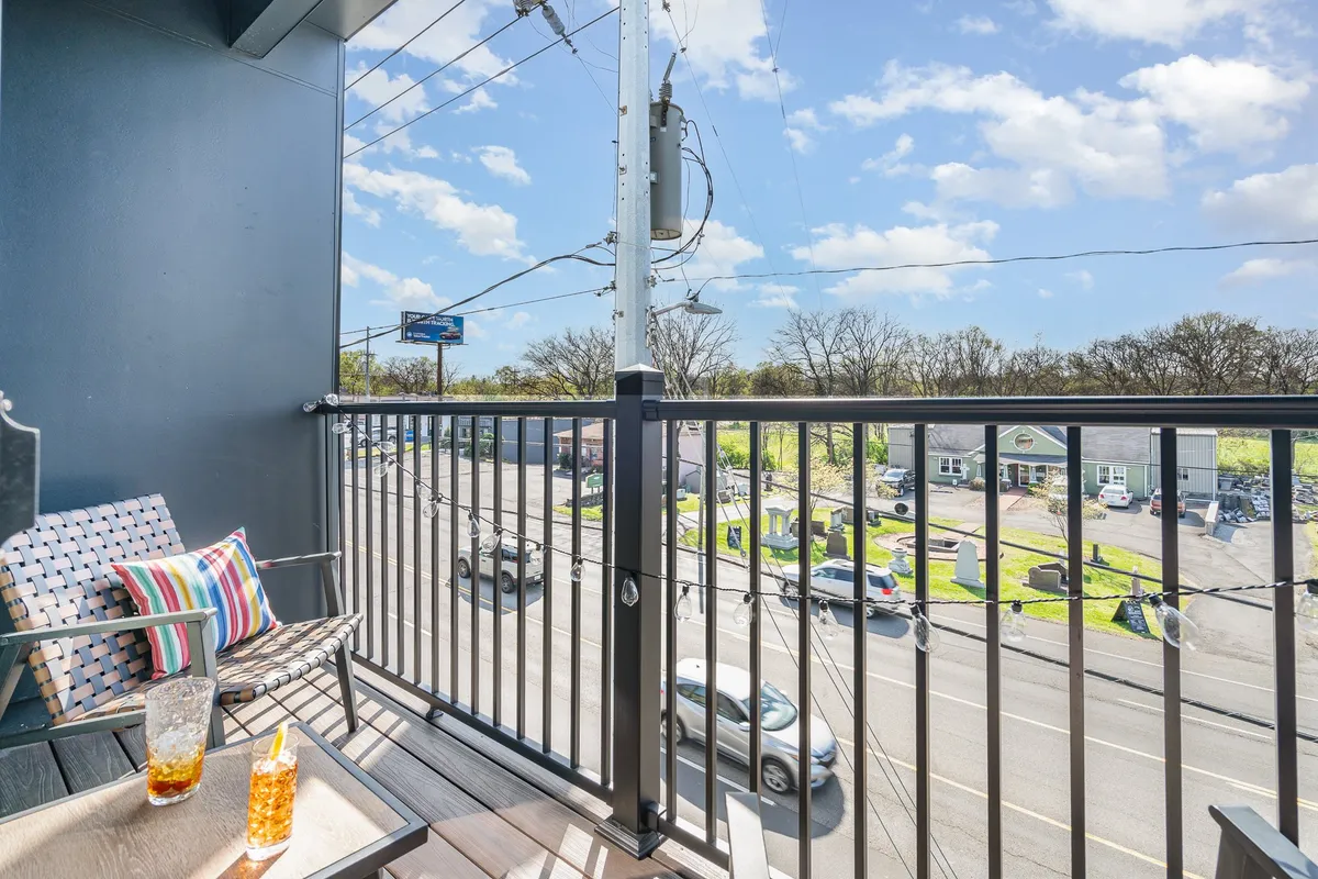 A cozy balcony setup featuring comfortable seating and a colorful drink, overlooking a vibrant street scene below. The setting is perfect for socializing, people-watching, and unwinding with friends while soaking in the urban atmosphere.