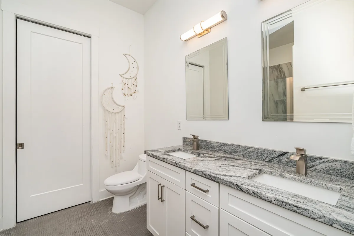 A modern bathroom with granite countertops, contemporary fixtures, and a decorative moon hanging, bathed in tranquil lighting. The space feels serene and inviting, ideal for personal grooming or a refreshing start to the day.